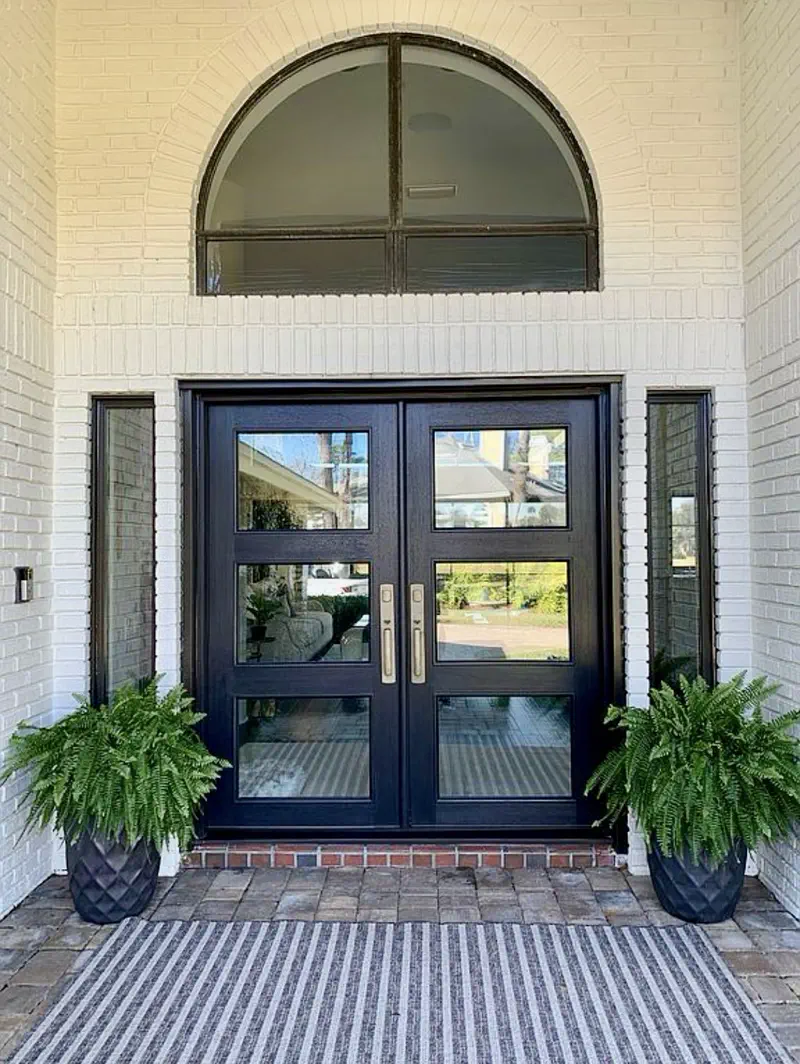 Black glass double doors with an arched transom, white painted brick and Boston ferns — brick front entry remodel after by All Beaches Remodeling and Repair