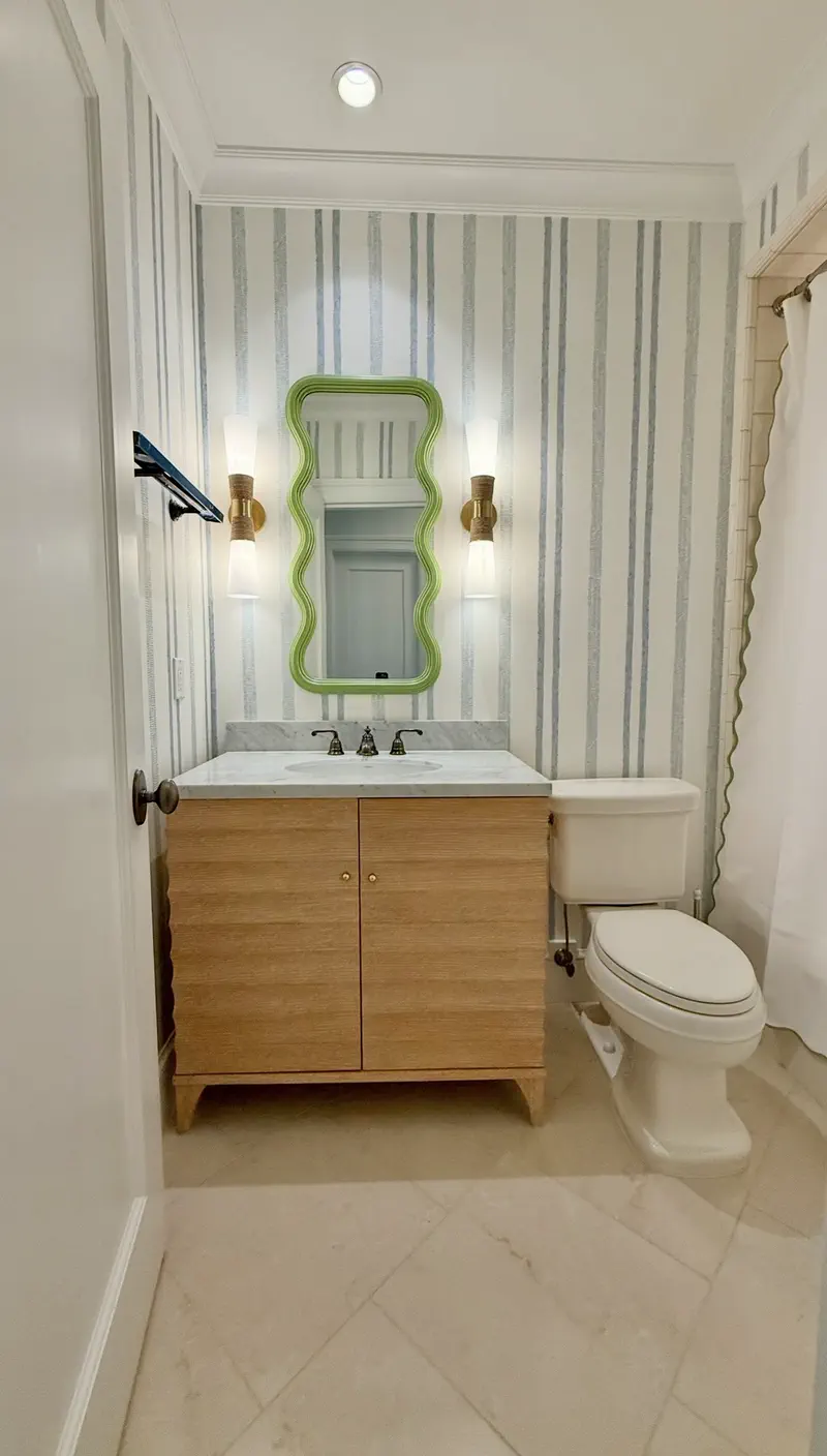 Powder room with blue-and-white striped wallpaper, a wood vanity, marble counter and a lime-green wavy mirror