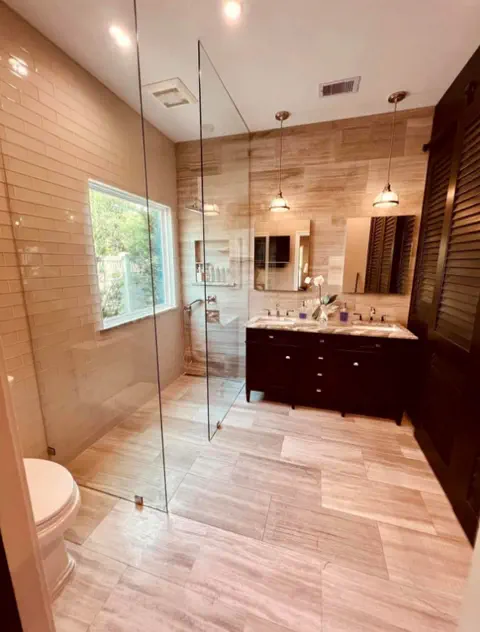 Bathroom with dark wood double vanity, marble-look counters, pendant lights and a frameless glass shower