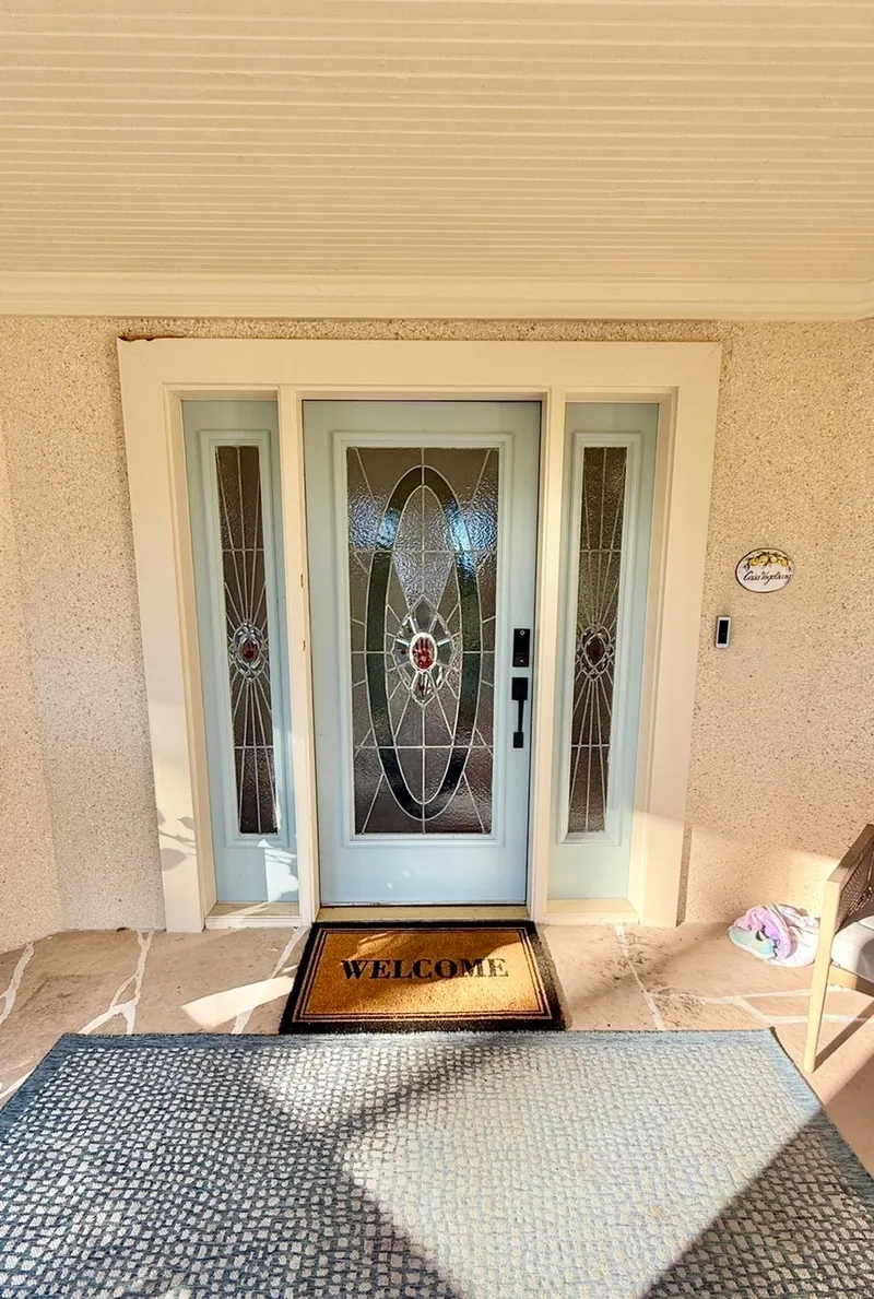 Front porch remodel before — light blue door with oval stained-glass insert and a blue rug by All Beaches Remodeling and Repair