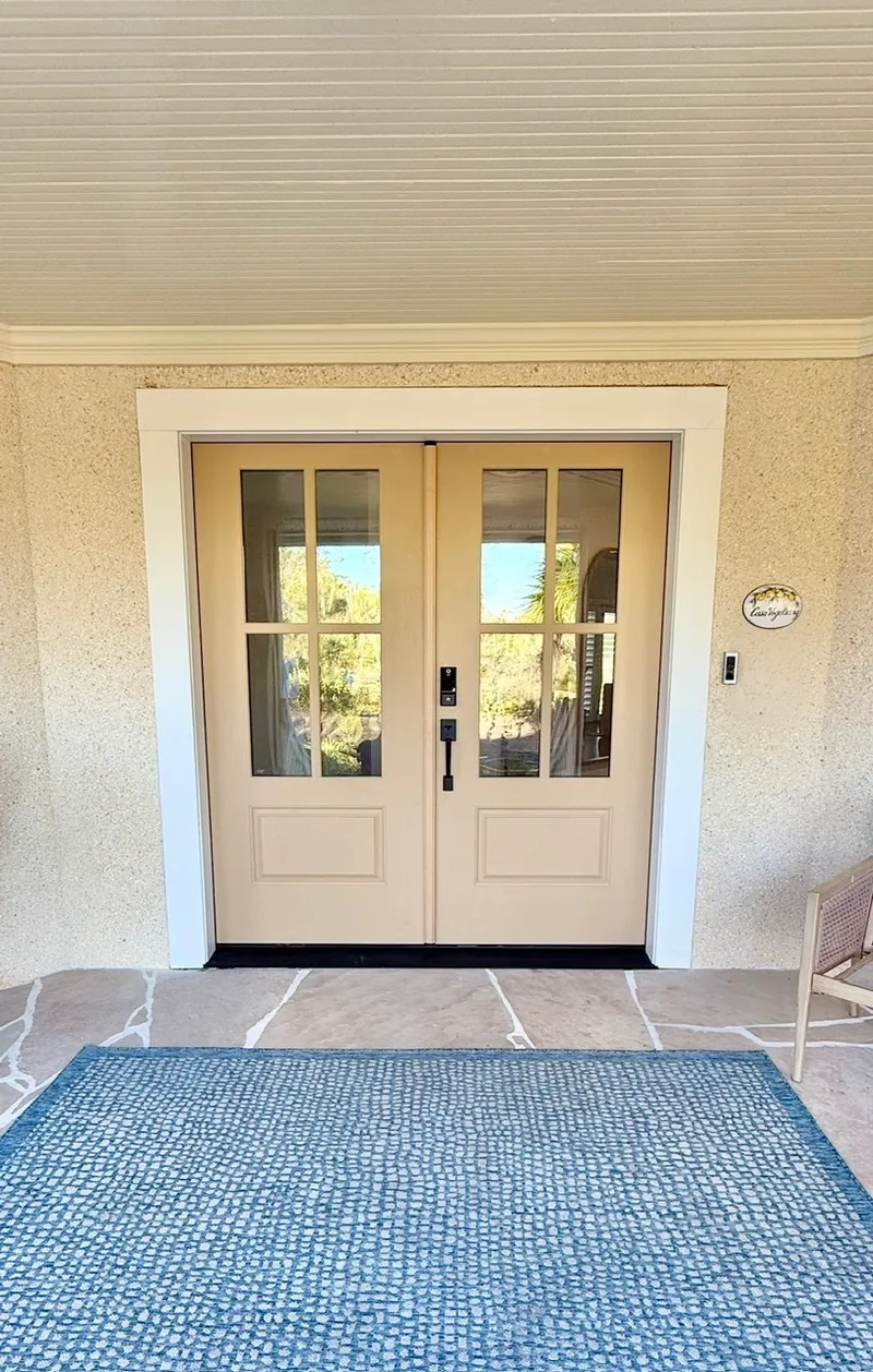 Front porch remodel after — tan double doors with 6-lite glass, black hardware and a blue rug by All Beaches Remodeling and Repair