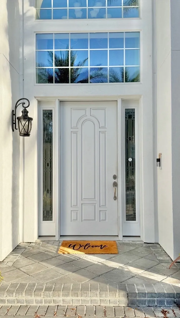 Front entry remodel before — white 8-panel single door with sidelites and a Welcome doormat by All Beaches Remodeling and Repair