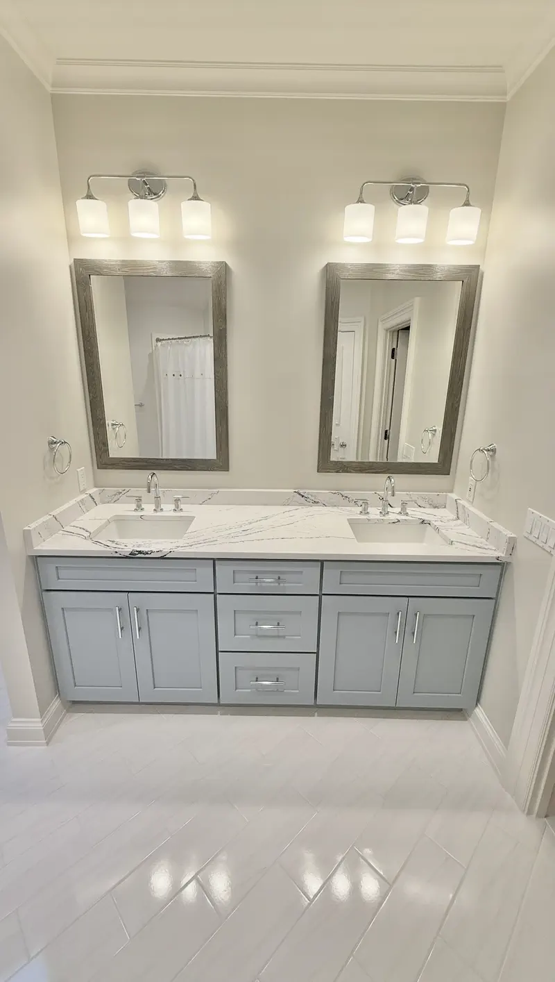 Bathroom with a light gray double vanity, marble-look quartz counters, wood-framed mirrors and chrome fixtures