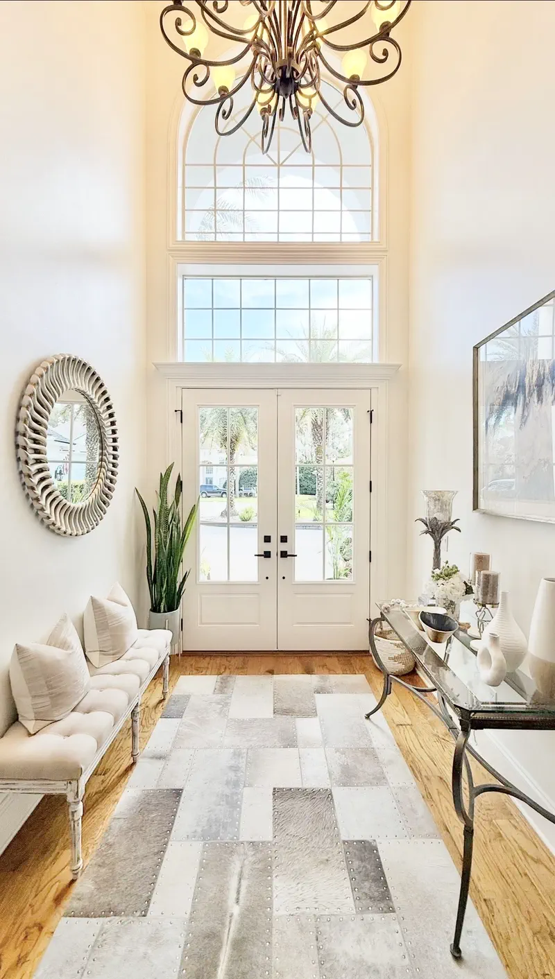 Interior foyer with white glass double doors, chandelier, tufted bench and cowhide rug