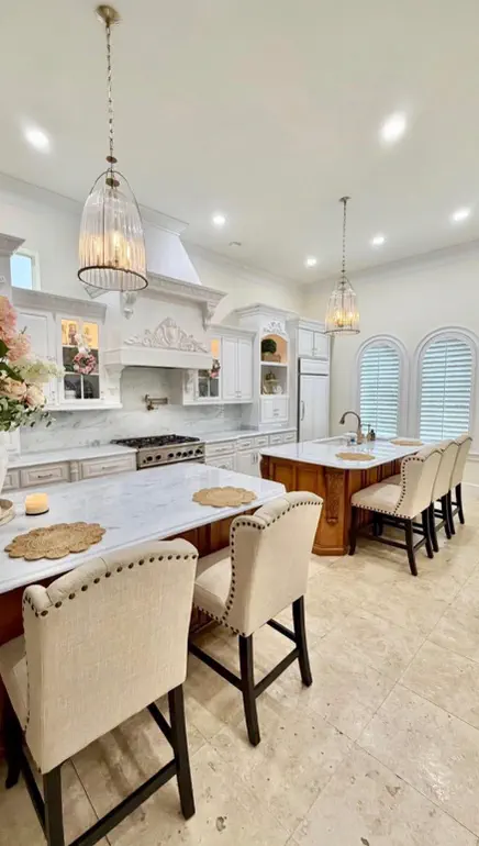 Finished kitchen with white custom cabinetry, marble islands with dark wood bases, and cream barstools in Northeast Florida