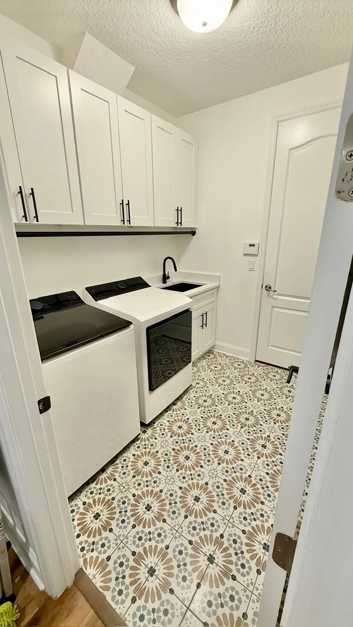 Laundry room remodel after — white shaker cabinets, black faucet and patterned medallion tile floor by All Beaches Remodeling and Repair