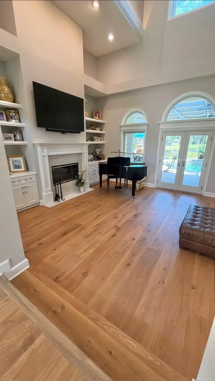 Living room remodel after — wide-plank wood floors, refinished fireplace, styled shelves and piano by All Beaches Remodeling and Repair
