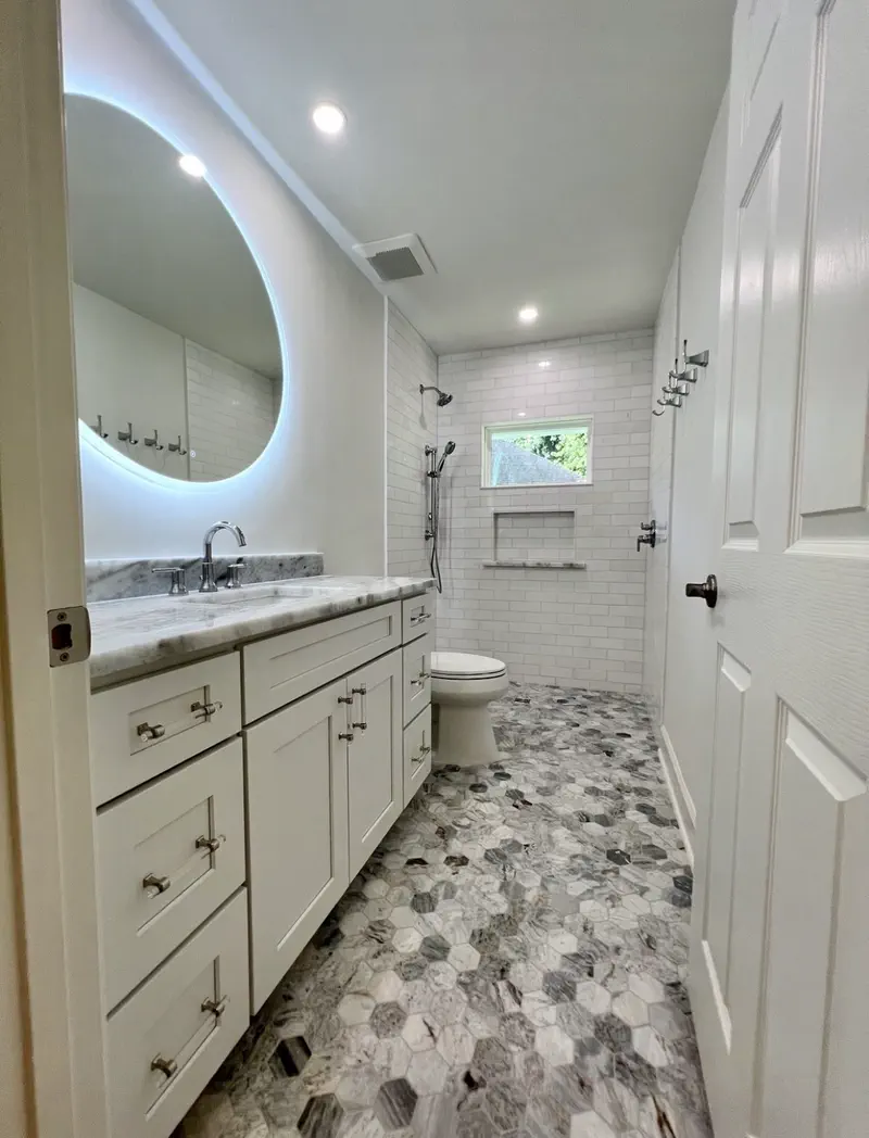 Marble walk-in shower with hexagonal marble floor, subway tile and a backlit circular mirror