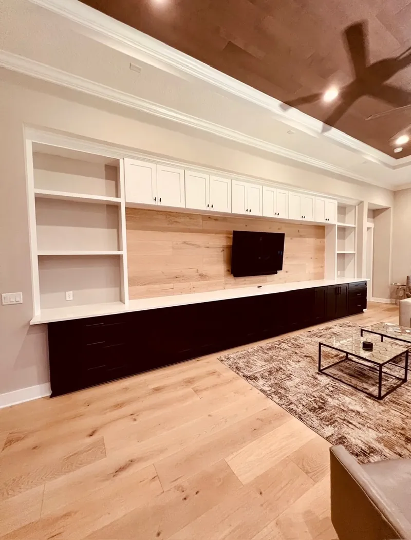 Media wall remodel after — custom built-ins with white upper cabinets, wood plank TV backdrop and black lower cabinets by All Beaches Remodeling and Repair