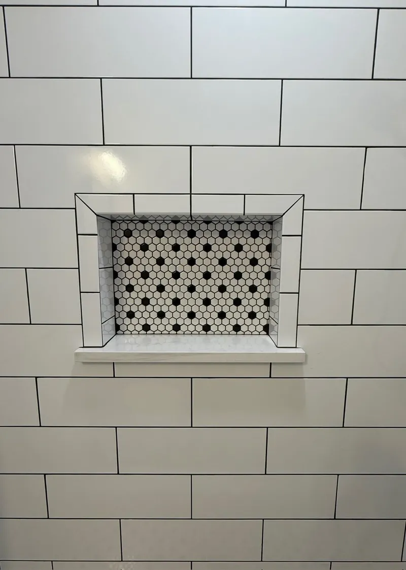 Recessed shower niche with black-and-white hexagon mosaic framed by white subway tile and black grout in Northeast Florida