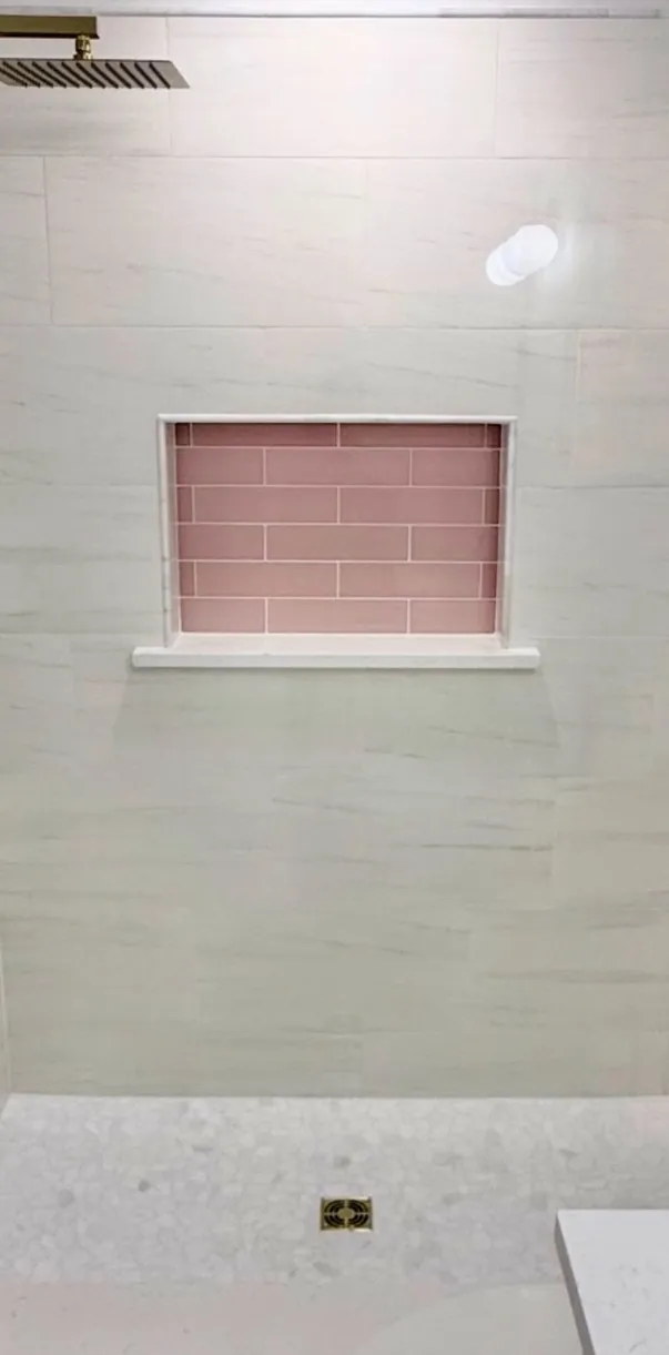 Recessed shower niche with pink subway tile and a gold rain shower head in a white marble-look tile shower in Northeast Florida