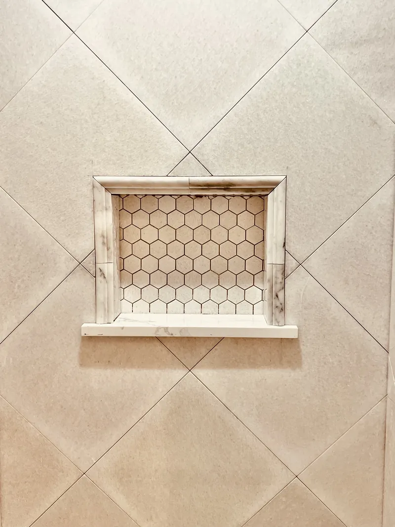 Finished marble hexagon mosaic shower niche with marble pencil trim and shelf in a diagonal-tile shower in Northeast Florida