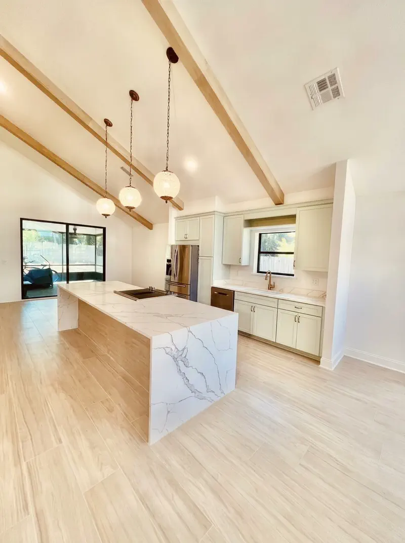 Finished kitchen remodel with vaulted wood beam ceiling, waterfall quartz island and custom sage cabinetry in Northeast Florida