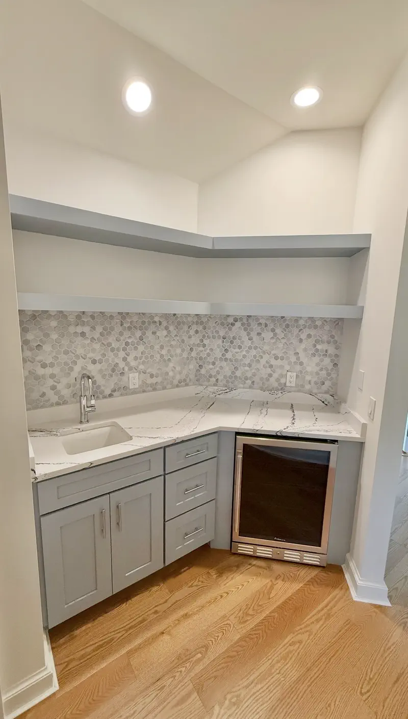L-shaped wet bar with blue-gray shaker cabinets, hexagonal marble backsplash, quartz counter and a glass-door beverage fridge