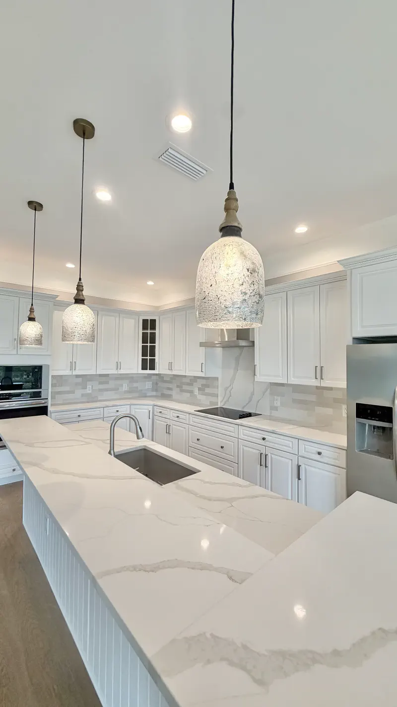 White galley kitchen with marble-look island, shaker cabinets and pendant lights by All Beaches Remodeling and Repair
